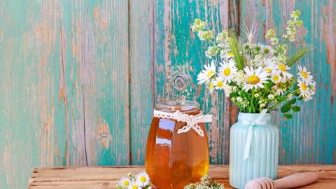 Blütenhonig im Glas neben Blumenstrauß